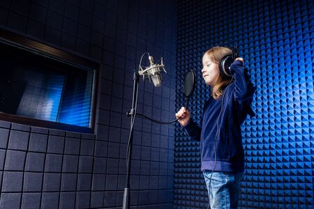 girl star singer artist in a black blouse with headphone recording new song with microphone.の写真素材