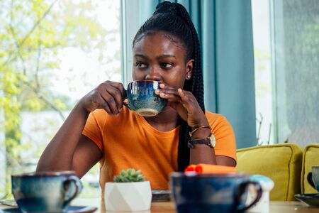 dark-skinned business woman in cafe, looking on screen of laptop standing drinking cup of coffee.の写真素材