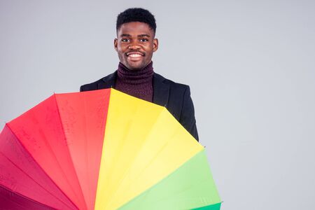 smiling businessman in suit coat wool with multi-coloured umbrella white background studioの写真素材