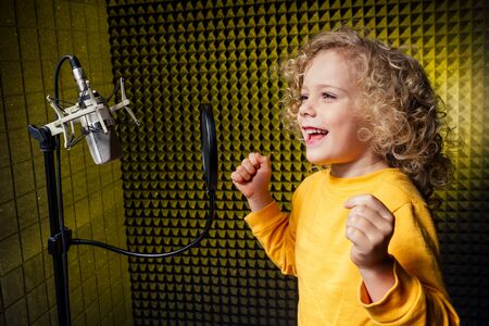 girl blonde curly hair style star singer artist in a yellow blouse with headphone recording new song with microphone.の写真素材