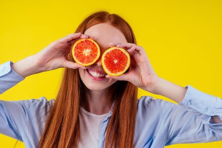 cheerful, redhaired ginger woman holding red orenge in studio yellow background,autumn vitamin immunity concept.の写真素材