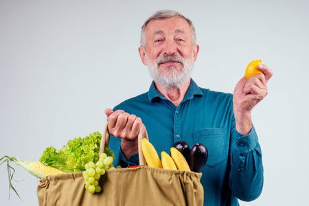 old senior grandfather holding cotton reusable shopper bag full of natural farmer vegetables:corn,bananas grapes, eggplant and grapes in studio white background. zero waste compostの写真素材