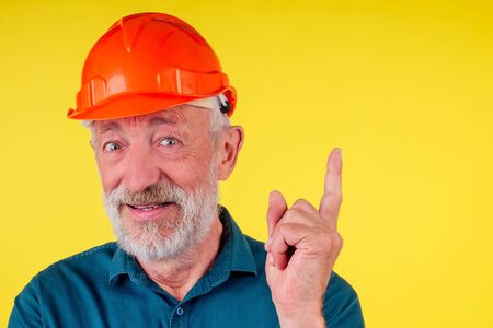 Elderly handsome painting the walls in new a new house with yellow paint,holding roller brush,studio nackground.pointing finger uo copyspaseの写真素材