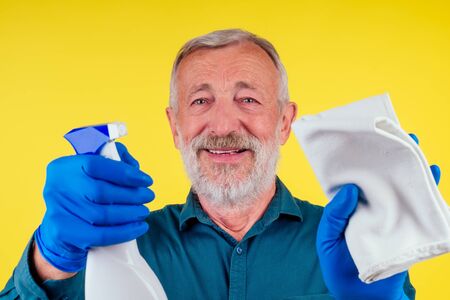 Portrait of a man with towel and spray ready to clean windows in studio yellow backgroundの写真素材