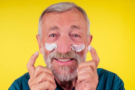 Smiling mature businessman in suit showing anti-aging lotion product . cheek pimple, whelk problem...