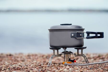 The pan with the porridge stands on the gas burner Camping Stove . On the background of the riverの写真素材