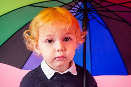 portrait of happy and beautiful little blond boy blue in black knitted blouse holding a colorful rainbow umbrella autumnal springtime season .charming child walking in the parkの写真素材