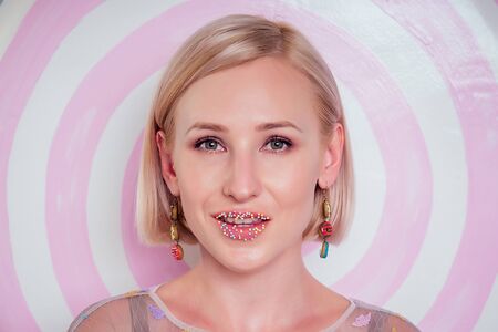 portrait of beautiful blonde Barbie woman confectionery sprinkling colorful sugar on lips...