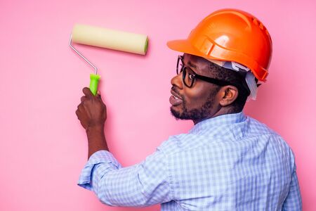 black man African American holding paint roller in hand paints the wall in pink color .happy african...