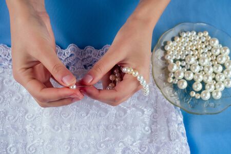 close-up hands of woman seamstress tailor dressmaker designer wedding dress sews pearl beads to lace on a blue background in the studioの写真素材