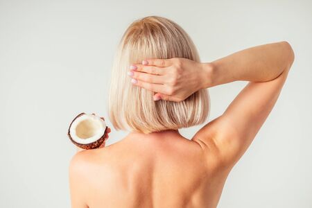 Beautiful young blonde hairstyle girl with a long eyelashes make-up and perfect skin with coconut in her hand in the studio on a white background. Beauty face hair care.の写真素材
