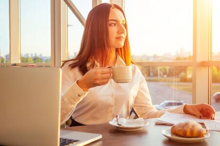 young business woman drinks coffee and works behind laptop with papersの写真素材