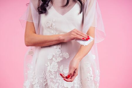 Woman bride in white dress part of the body of a young woman in a pink studio . girl using wet wipes...