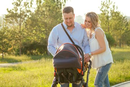 beautiful and young woman mother handsome man and baby in a stroller walking in the park