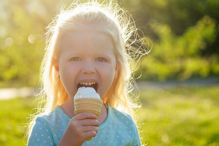 cute little blonde girl daughter eating vanilla ice cream in the parkの写真素材
