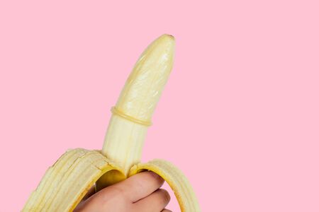 close up of womans hands putting banana on condom cock on a pink background in the studio.sexual intimate games safe sexの写真素材