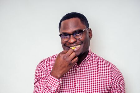 handsome and young african american male model in a plaid pink shirt and stylish glasses eating...