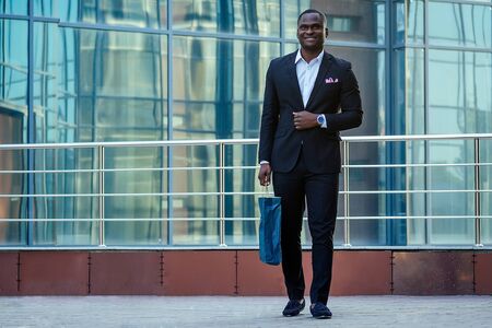 handsome and stylish African American man in a fashionable black jacket and a white shirt with a collar with a elegant tie posing background of Manhattan glass offices cityscapeの写真素材