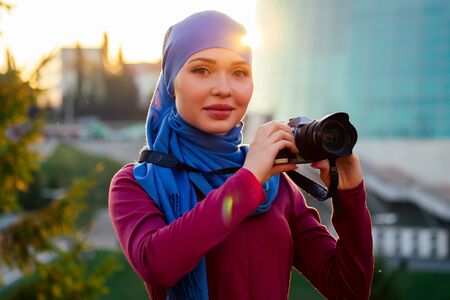 Female photographer wearing a hijab. woman holding a camera hobbyist or a journalist in summer park...
