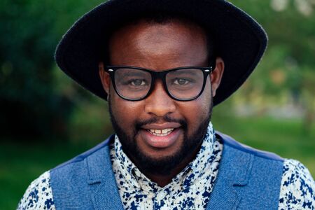 portrait of black men in stylish suits and black hat with glasses in a summer park....