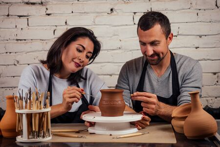 happy family on a creative joint vacation. romantic couple in love working together on potter wheel and sculpting clay pot,a bearded man and a young woman mold a vase in craft studio workshop.の写真素材
