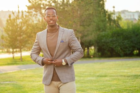 a young and handsome stylish model afro- american man in a stylish suit in a summer park . latino...