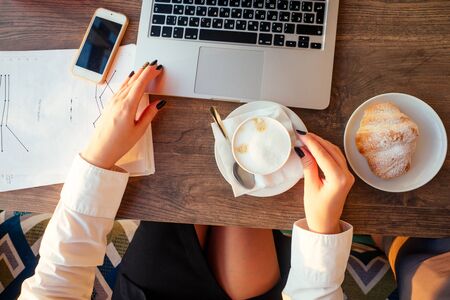 young business woman drinks coffee and works behind laptop with papers.の写真素材