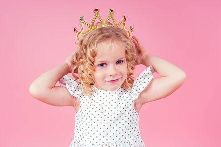 little girl beauty queen blue eyes, curls blonde hairstyle with a tiara crown on her head in a cute white dress in peas posing in the studio on a pink background.birthday celebration,Beauty contestの写真素材