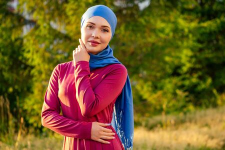 Islamic beautiful woman in a Muslim virgin dress standing on a summer park street background forest autumn treesの写真素材