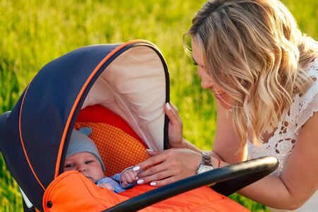 beautiful and young blonde mom taking care of baby in a stroller toddler