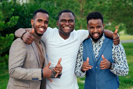 a group of three black men in stylish suits a meeting in a summer park. African-Americans friends hispanic businessman greeting pose teamwork outdoorsの写真素材