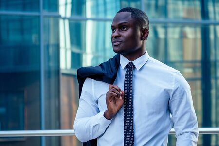 handsome and stylish African American model man in a fashionable black jacket and a white shirt with a collar with a elegant tie posing background of Manhattan glass offices cityscapeの写真素材