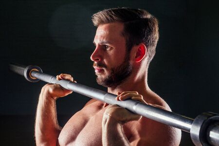 Muscular fitness man antique statue perfect muscles six pack abs and bare nude chest bodybuilder Apollo model bodybuilder makes exercise barbell for biceps in the gym on a black backgroundの写真素材