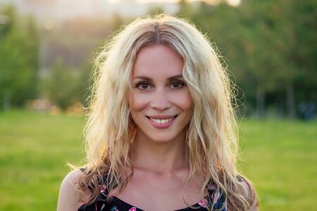 beautiful curly blonde happy young toothy smile girl in the summer park sunset rays field background