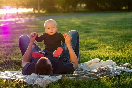 little baby boy together with his father play and develop on a blanket in the park in summerの写真素材