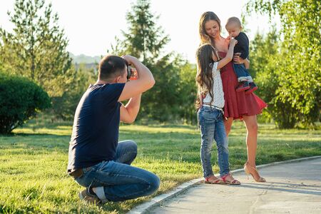 happy family is resting in the park in summer . beautiful mother , handsome father with a little baby boy and cute daughter photographed on camera . family photo shoot male photographerの写真素材