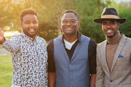 a group of three black men in stylish suits in a summer park. African-Americans friends hispanic...