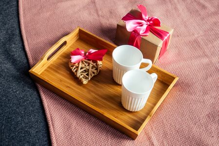 two white ceramic cups on a wooden tray and a box with a gift on the bed top view, copy space. romantic composition. Concept Valentine day holiday home morning natural light.の写真素材