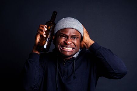 african american man holding a bottle of wine and feeling headache shit in studio black background.bum homeless drowning out the painの写真素材