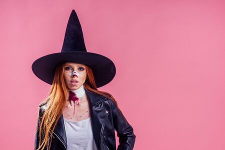 redhaired ginger girl dressed with a huge witch hat and black leather jacket ,spooky blood make up...