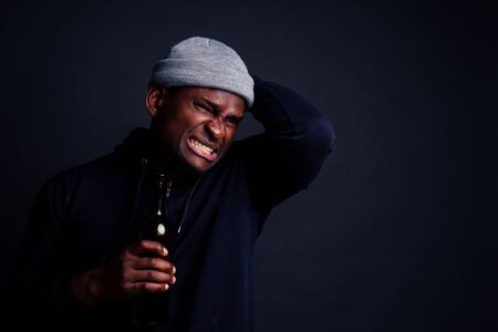 african american man holding a bottle of wine and feeling headache in studio black background.bum...