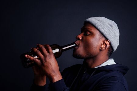 african american gue wearing gray hat and hoody hjlding botle with wine in srudio black...