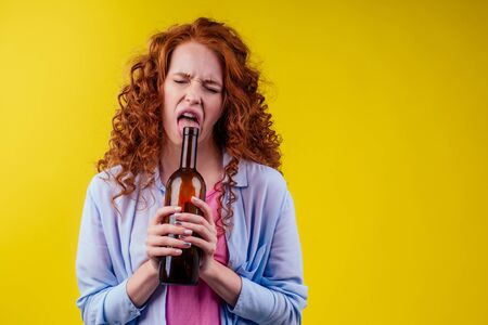 curly redhead ginger woman drinking beer and feeling bad mood in csudio yellow background