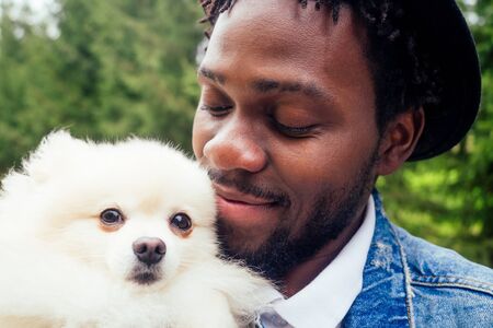 afro man hugging his fluffy spitz in parkの写真素材