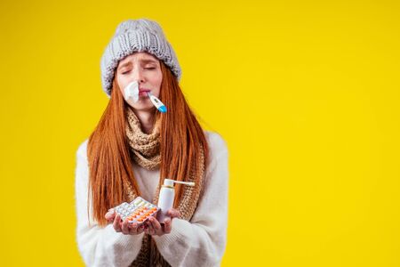 unwell redhaired ginger woman runny nose wearing knitted sweater and scarf with many pills in hand...