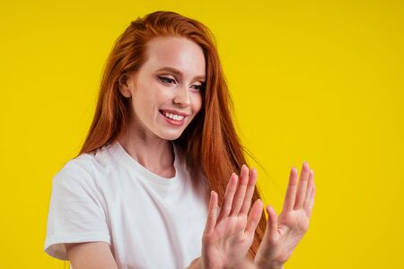 redhead ginger woman enjoying fresh manicure on studio yellow background
