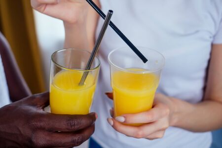 international couple in love holding in hands glasses with orange juice.afro man use disposable...