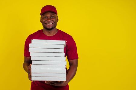 African-american delivery man with package wearing red T-shirt and cap in studio yellow background....