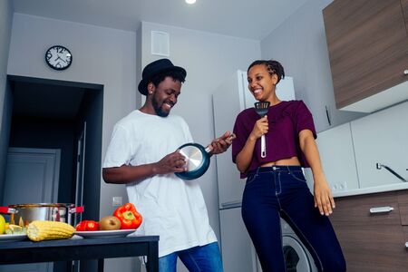 Beautiful young Afro American couple is smiling while dancing in kitchenの写真素材