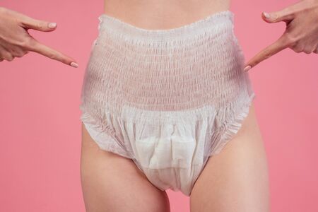 young redhaired ginger woman wearing incontinence diaper in studio pink backgroundの写真素材